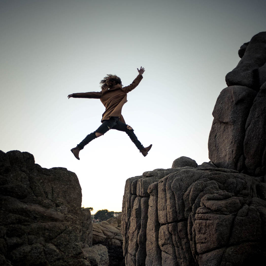 woman in mid-air courageously leaping through rock mountains symbolizing the practice of courage in our daily lives